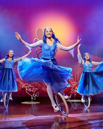 Three acrobats dressed in blue fairies costumes performing a unicycle act. 